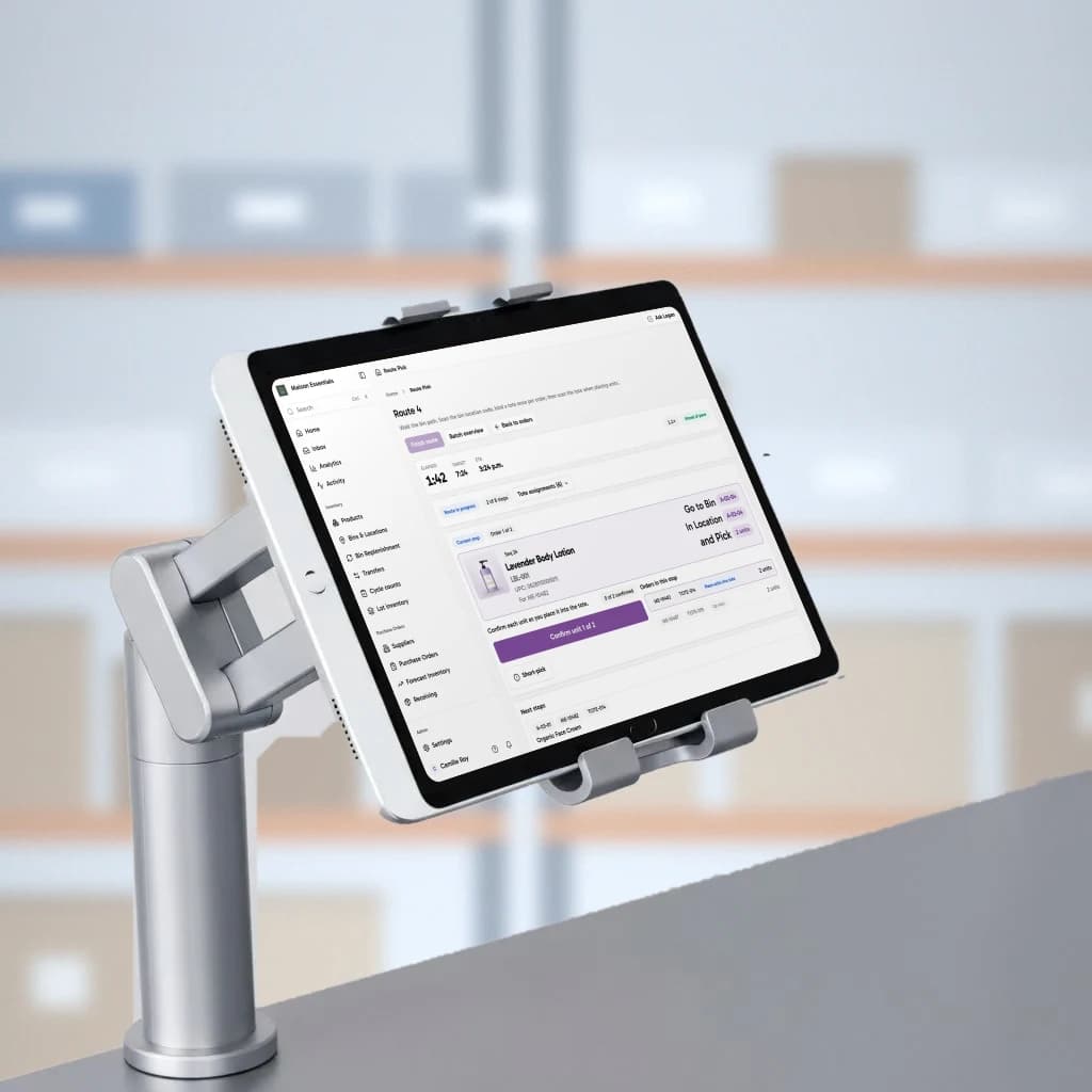 An iPad running Logentic's pick route screen on an aluminum pack station mount, in a warehouse